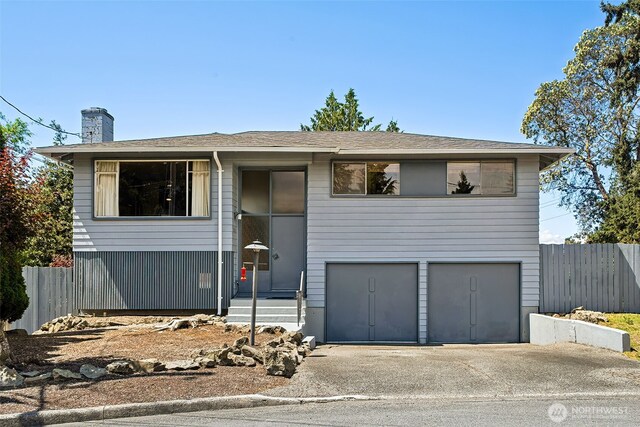split foyer home with an attached garage, fence, driveway, a chimney, and roof with shingles