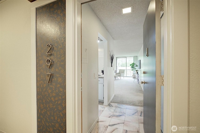 hall featuring light marble finish floors, a textured ceiling, and baseboards