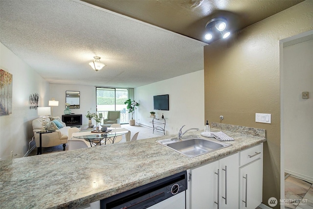 kitchen with a sink, white dishwasher, white cabinets, light countertops, and a textured ceiling