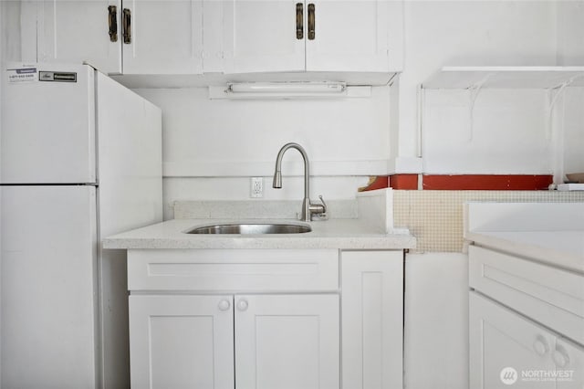 kitchen featuring freestanding refrigerator, a sink, white cabinets, and light stone countertops