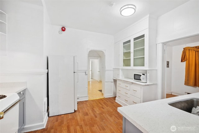 kitchen with white appliances, white cabinetry, light wood finished floors, and glass insert cabinets