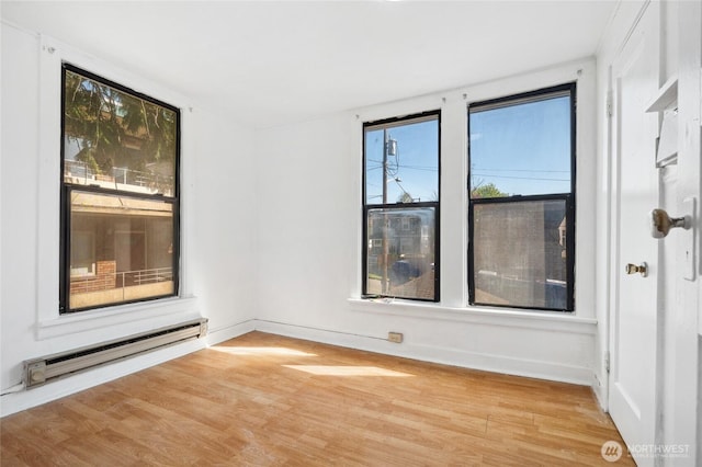 unfurnished room featuring baseboard heating, wood finished floors, and baseboards