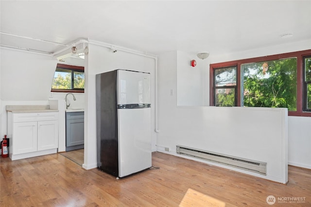 kitchen featuring freestanding refrigerator, a baseboard radiator, light wood-style flooring, and a sink