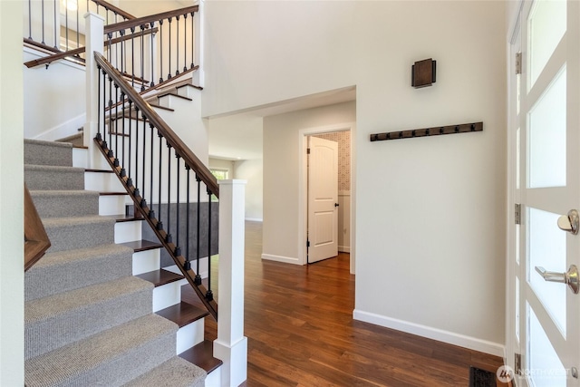 stairs with baseboards, wood finished floors, and a high ceiling