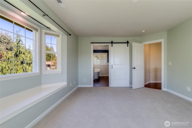 unfurnished bedroom featuring carpet flooring, a barn door, and baseboards