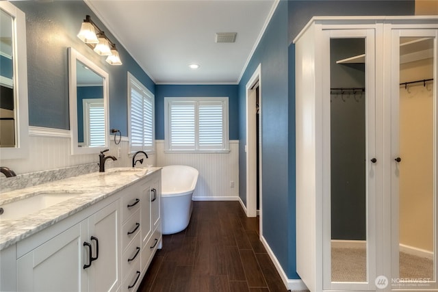 full bathroom with wainscoting, a freestanding tub, double vanity, wood finished floors, and a walk in closet