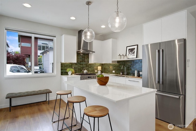 kitchen featuring high end fridge, wall chimney exhaust hood, a sink, a kitchen island, and a breakfast bar