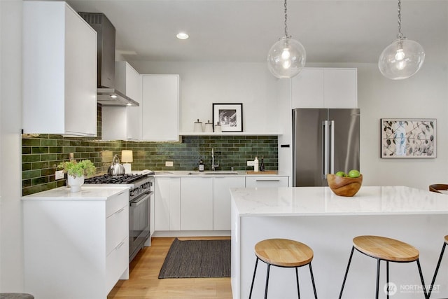 kitchen with high end appliances, a sink, a kitchen breakfast bar, wall chimney range hood, and tasteful backsplash