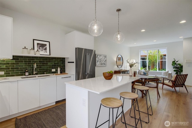 kitchen featuring high end refrigerator, a sink, a kitchen bar, light countertops, and white cabinetry