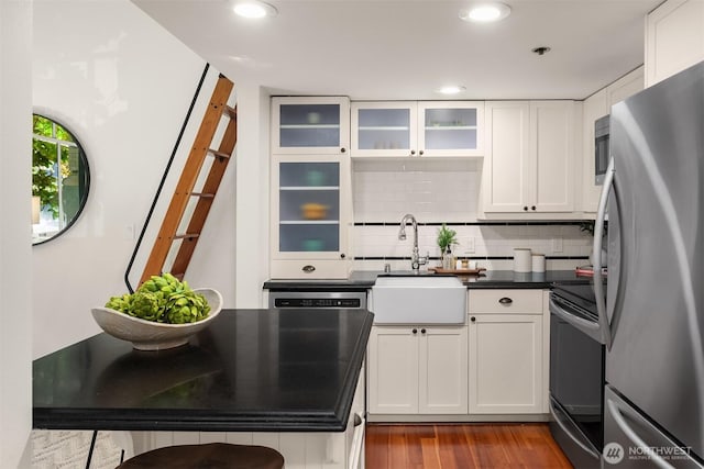 kitchen with stainless steel appliances, a sink, dark wood finished floors, white cabinets, and dark countertops