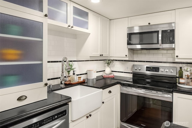 kitchen with stainless steel appliances, a sink, backsplash, white cabinetry, and dark countertops