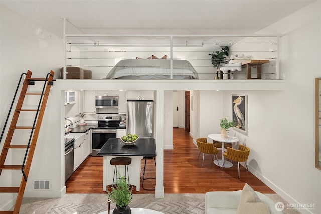 kitchen with appliances with stainless steel finishes, dark countertops, white cabinets, and wood finished floors