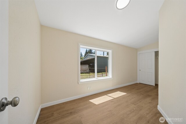 unfurnished bedroom with wood finished floors, baseboards, and lofted ceiling