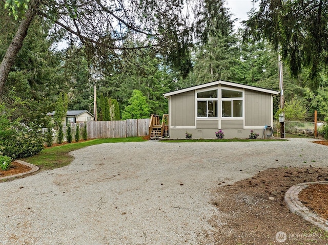 view of outbuilding with gravel driveway, fence, and view of scattered trees