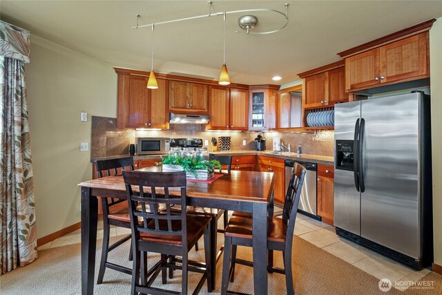 7806 Birch Bay Dr Unit 515, Blaine, WA 98230 - kitchen featuring stainless steel appliances, under cabinet range hood, tasteful backsplash, brown cabinetry, and decorative light fixtures
