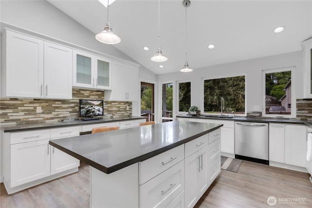 kitchen featuring stainless steel dishwasher, a sink, dark countertops, lofted ceiling, and backsplash