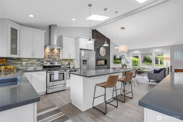 kitchen with stainless steel appliances, wall chimney range hood, a kitchen breakfast bar, a skylight, and white cabinets