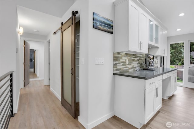 kitchen with a barn door, dark countertops, light wood-style floors, tasteful backsplash, and white cabinets