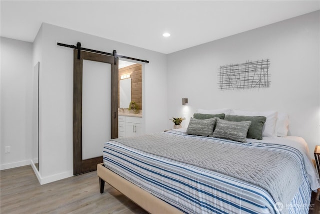bedroom featuring a barn door, light wood-style flooring, baseboards, recessed lighting, and ensuite bath