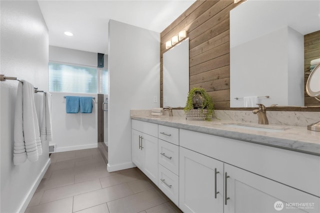 bathroom with wooden walls, a stall shower, double vanity, tile patterned flooring, and baseboards