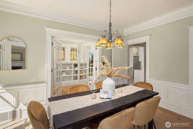 dining area featuring a chandelier, a decorative wall, crown molding, wood finished floors, and wainscoting