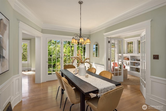 dining area featuring a chandelier, a decorative wall, crown molding, wainscoting, and light wood-style flooring