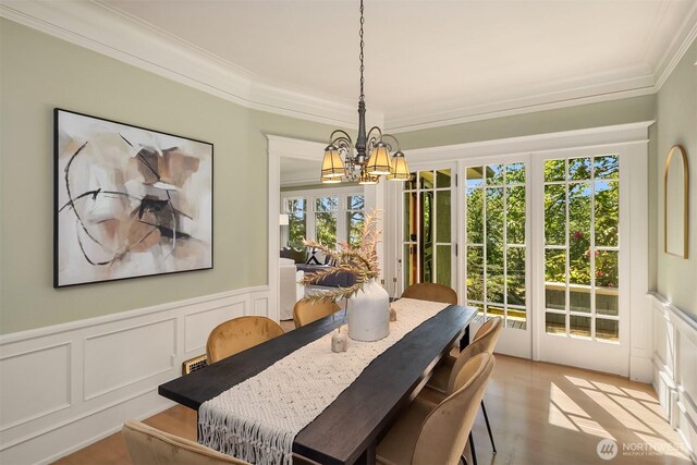 dining space with ornamental molding, a chandelier, a decorative wall, wainscoting, and light wood-type flooring