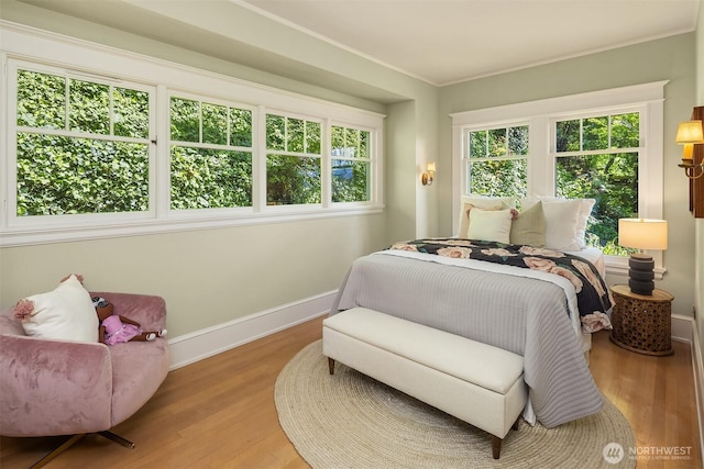 bedroom with wood finished floors, multiple windows, baseboards, and crown molding