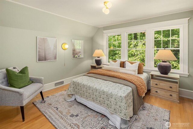 bedroom with baseboards, vaulted ceiling, and light wood finished floors