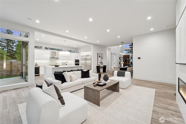 living room with light wood finished floors, recessed lighting, a glass covered fireplace, and baseboards