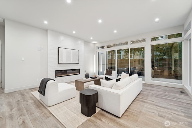 living room with light wood-type flooring, a large fireplace, and recessed lighting