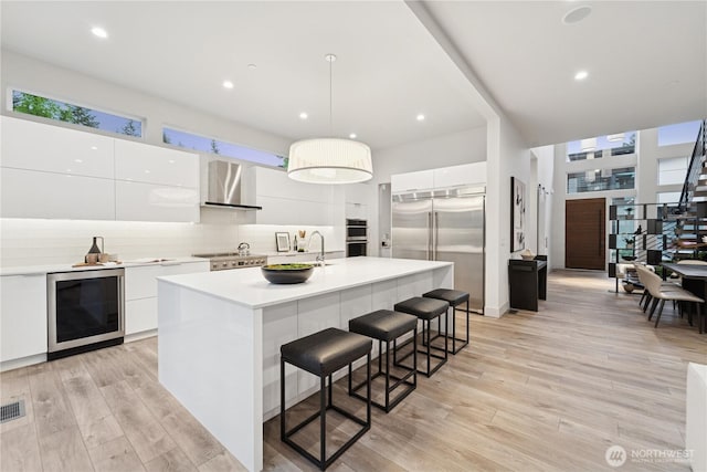 kitchen featuring wine cooler, modern cabinets, wall chimney range hood, stainless steel appliances, and white cabinetry