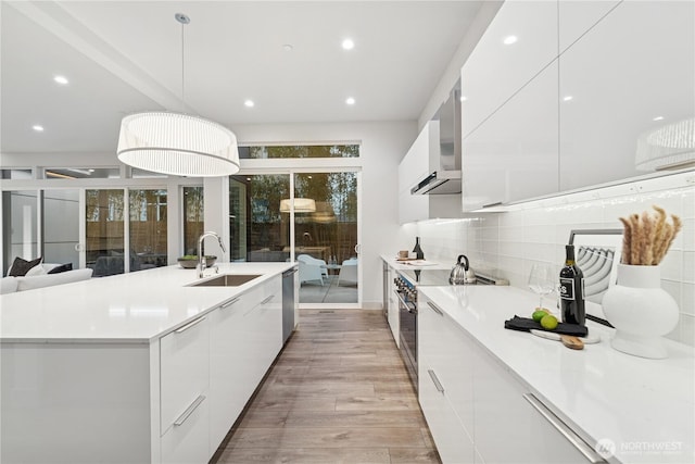 kitchen featuring modern cabinets, a sink, white cabinetry, wall chimney range hood, and light countertops