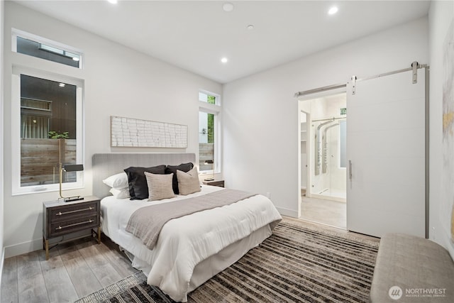bedroom featuring light wood-style flooring, a barn door, recessed lighting, baseboards, and connected bathroom