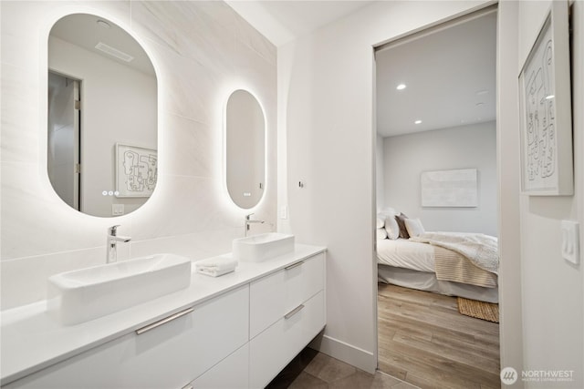 ensuite bathroom featuring double vanity, wood finished floors, and recessed lighting