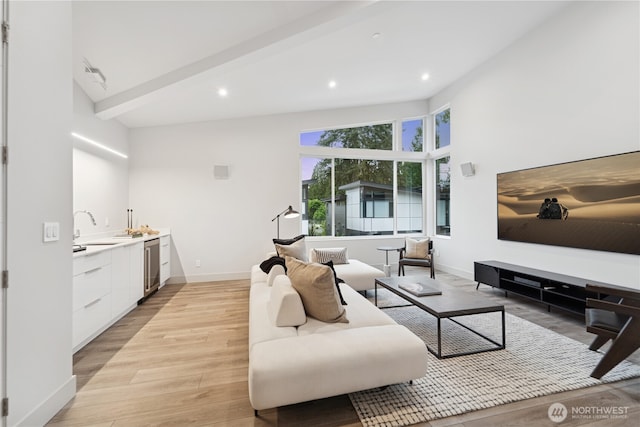 living area with light wood-style floors, baseboards, recessed lighting, bar with sink, and beam ceiling