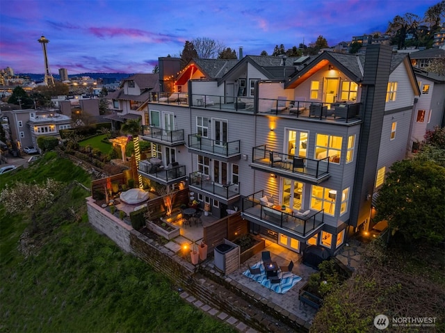 1416 6th Ave N, Seattle, WA 98109 - back of house at dusk with a balcony, a patio area, a chimney, an outdoor fire pit, and an in-ground hot tub