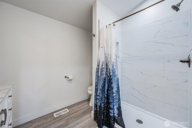 bathroom featuring tiled shower, toilet, wood finished floors, vanity, and baseboards