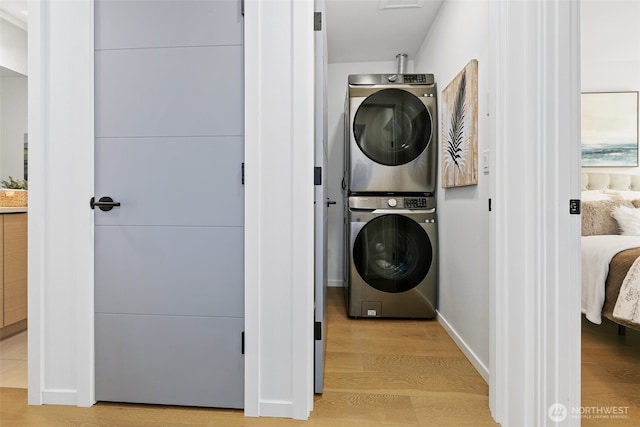 laundry area with stacked washer and clothes dryer, light wood finished floors, and baseboards