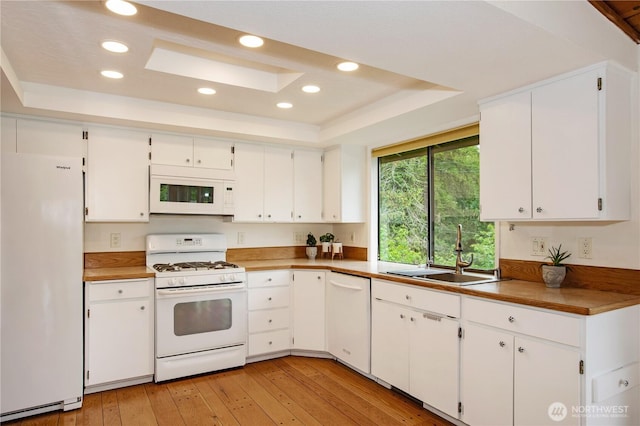kitchen with white appliances, a sink, a tray ceiling, white cabinets, and recessed lighting