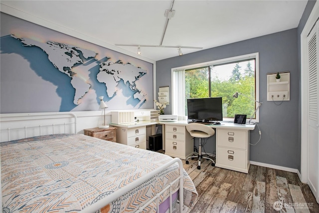 bedroom featuring wood finished floors, track lighting, baseboards, a closet, and an office area