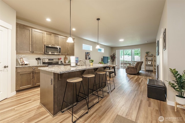 7135 S 13th St, Ridgefield, WA 98642 - kitchen with appliances with stainless steel finishes, open floor plan, a breakfast bar area, light wood-type flooring, and light stone counters