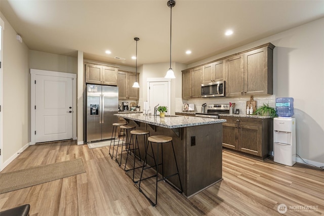 7135 S 13th St, Ridgefield, WA 98642 - kitchen with appliances with stainless steel finishes, light wood finished floors, a kitchen bar, tasteful backsplash, and light stone countertops