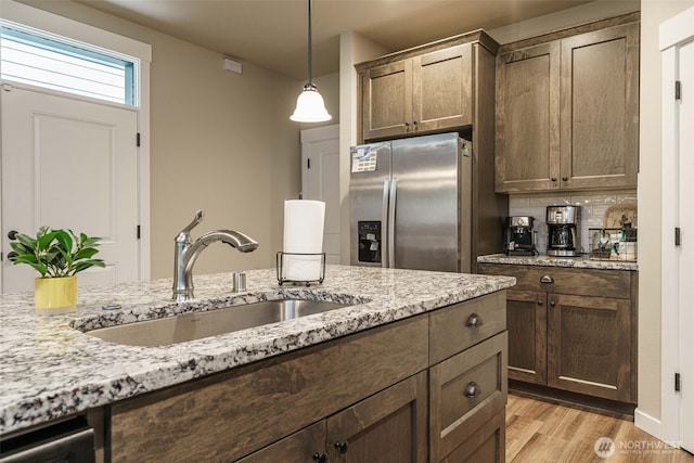 7135 S 13th St, Ridgefield, WA 98642 - kitchen featuring stainless steel refrigerator with ice dispenser, a sink, light wood-style floors, decorative light fixtures, and light stone counters