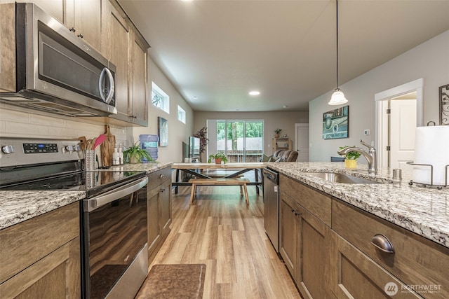 7135 S 13th St, Ridgefield, WA 98642 - kitchen featuring appliances with stainless steel finishes, a sink, light wood finished floors, light stone counters, and hanging light fixtures