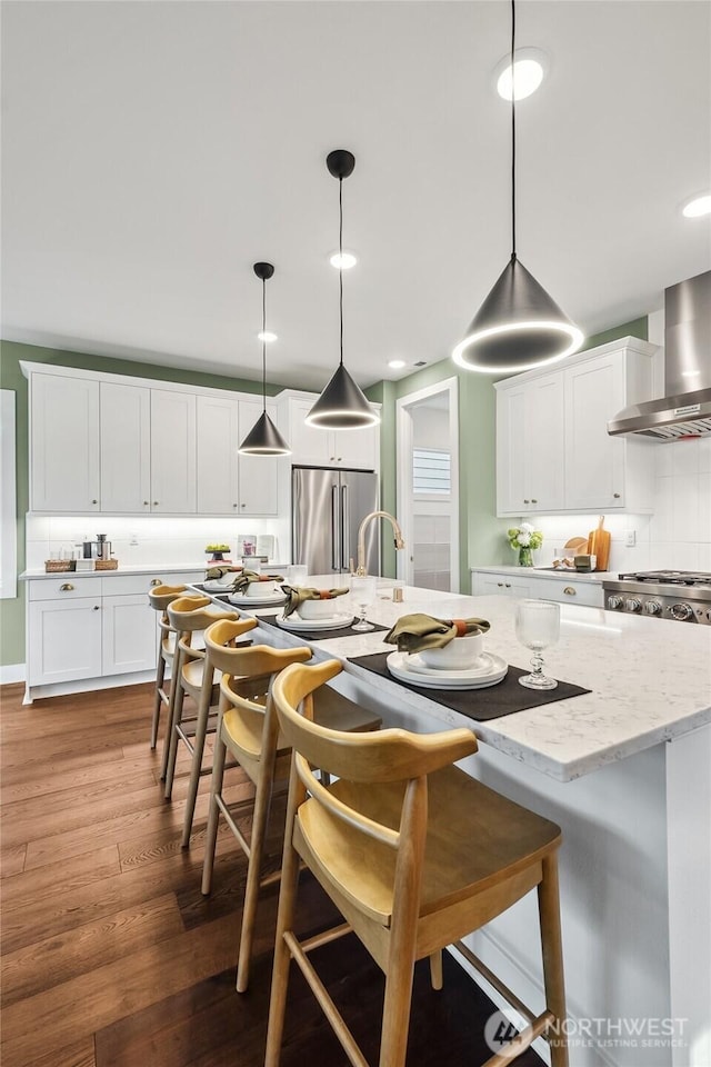 14652 203rd Ave E Unit 15, Bonney Lake, WA 98391 - kitchen featuring wall chimney exhaust hood, high end fridge, wood finished floors, a breakfast bar area, and white cabinetry