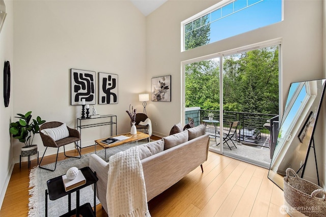 living room with a towering ceiling, light wood-style flooring, and baseboards