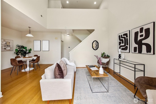 living room with a towering ceiling, light wood-style floors, stairs, baseboards, and recessed lighting