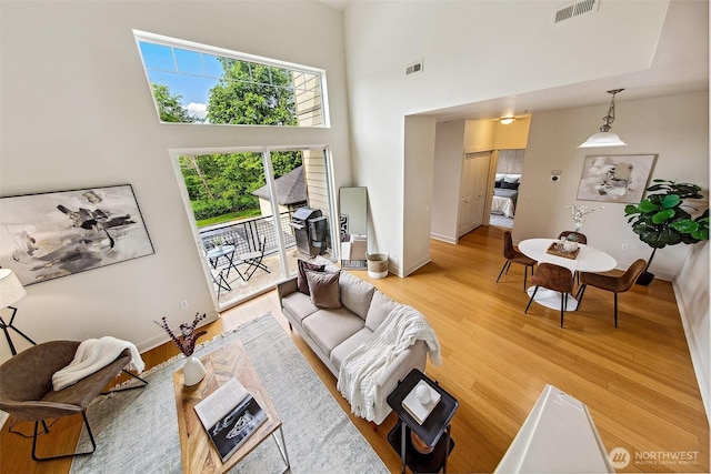 living area featuring light wood-type flooring, baseboards, and a towering ceiling