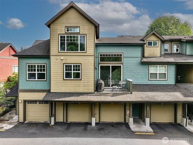 townhome / multi-family property featuring a balcony, asphalt driveway, an attached garage, and a shingled roof